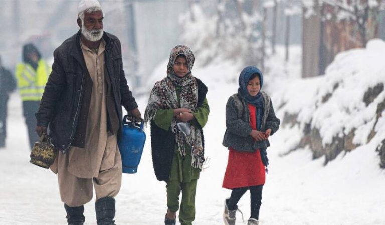 A man carrying gas canisters walks next to children along a street during snow fall in Kabul on January 11, 2023. (Photo by Wakil KOHSAR / AFP)