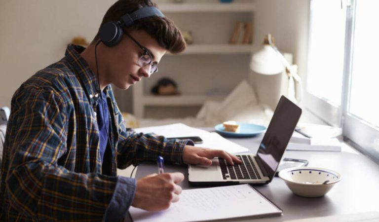 Teenage boy wearing headphones works at desk in his bedroom