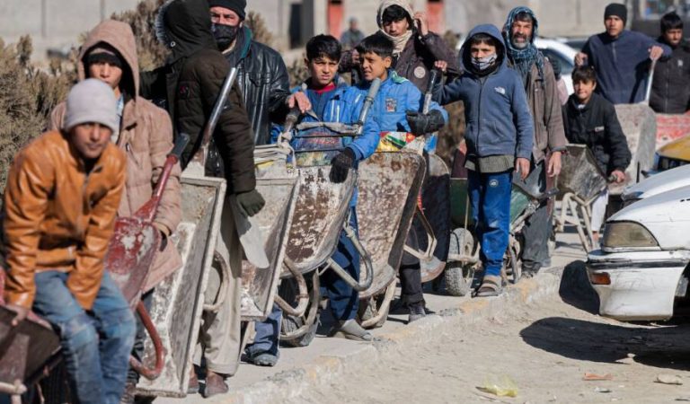 In this picture taken on January 3, 2023, Afghan boys with their wheelbarrows stand in a queue as they wait to receive food aid from a non-governmental organisation (NGO) in Kabul. - Aid groups say they have been "pushed against a wall" by the Taliban prohibiting Afghan women from working for NGOs, an injunction that has created a dangerous gap in life-saving support.  - To go with 'Afghanistan-Women-Aid', FOCUS by Estelle Emonet and Jay Deshmukh (Photo by Wakil KOHSAR / AFP) / To go with 'Afghanistan-Women-Aid', FOCUS by Estelle Emonet and Jay Deshmukh (Photo by WAKIL KOHSAR/AFP via Getty Images)