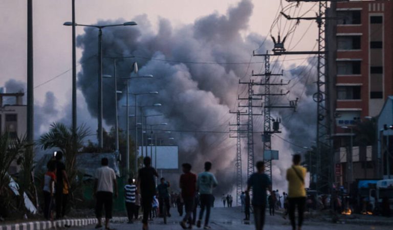 DEIR AL-BALAH, GAZA - JUNE 6: Palestinians stand on a road as black smoke rises over a building following the Israeli attacks in Deir al-Balah, Gaza on June 6, 2024. (Photo by Ali Jadallah/Anadolu via Getty Images)