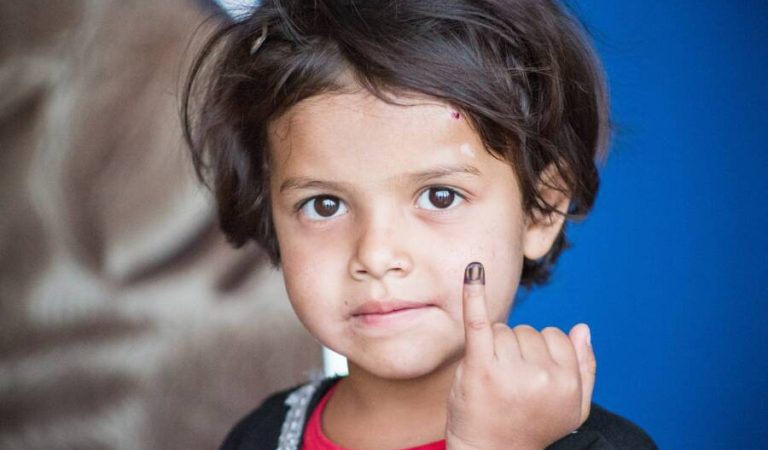 Shokria, a four-year child who has received the polio vaccination, is pointing his finger at the camera.