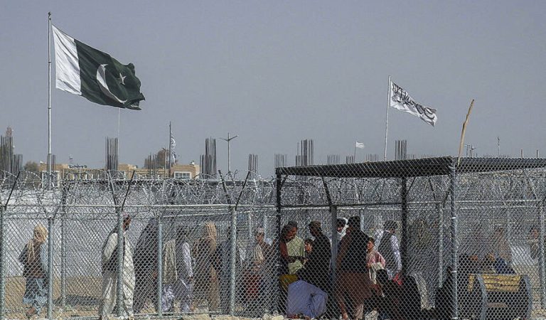 Afghan and Pakistani nationals walk through a security barrier to cross the border as a national flag of Pakistan and a Taliban flag is masted in the Pakistan-Afghanistan border crossing point in Chaman on August 24, 2021, following Taliban's military takeover of Afghanistan. (Photo by - / AFP)