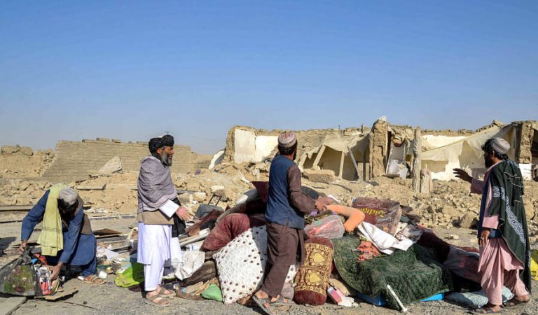 Afghan people stand along with belongings outside their damaged house in the Spin Boldak district of Kandahar province on October 16, 2025, a day after the cross-border clashes between Afghanistan and Pakistan. A ceasefire along the frontier between Afghanistan and Pakistan was holding on October 16, officials on both sides said, after dozens of troops and civilians were killed in cross-border clashes. (Photo by Sanaullah SEIAM / AFP via Getty Images)
