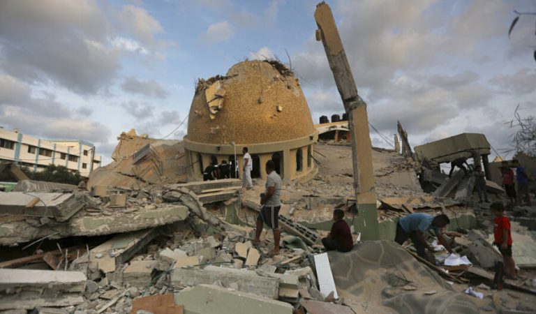 People stand outside a mosque destroyed in an Israeli air strike in Khan Younis, Gaza Strip, Sunday, Oct.8, 2023. The Hamas militants broke out of the blockaded Gaza Strip and rampaged through nearby Israeli communities, taking captives, while Israel's retaliation strikes leveled buildings in Gaza. (AP Photo/Yousef Masoud)