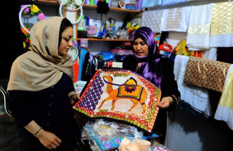 In this picture taken on June 2, 2014, Afghan shoppers examine a silk cloth to buy in a women's business centre in the city of Herat province. Once a stop along the Silk Road trade route, western Afghanistan has a long tradition of producing silk used to weave carpets, a process that dates back thousands of years. Carpets are Afghanistan's best-known export, woven mostly by women and children in the north of the country, a trade which once employed, directly or indirectly, six million people, or a fifth of the country's population, although that figure has dropped sharply. In cooperation with a non-profit organisation the Department of Agriculture in Herat provided some 5,050 silkworm boxes to several districts at the beginning of 2014 to revive silk production in the region. Some 42,500 women and their families are involved in the project which aims to provide a means of subsistence and potentially lead to international market access for silk producers in the country. The popular wool and silk Afghan carpets made by different tribes can sell for a price that can range between 150 USD to thousands of dollars. AFP PHOTO/Aref Karimi        (Photo credit should read Aref Karimi/AFP via Getty Images)