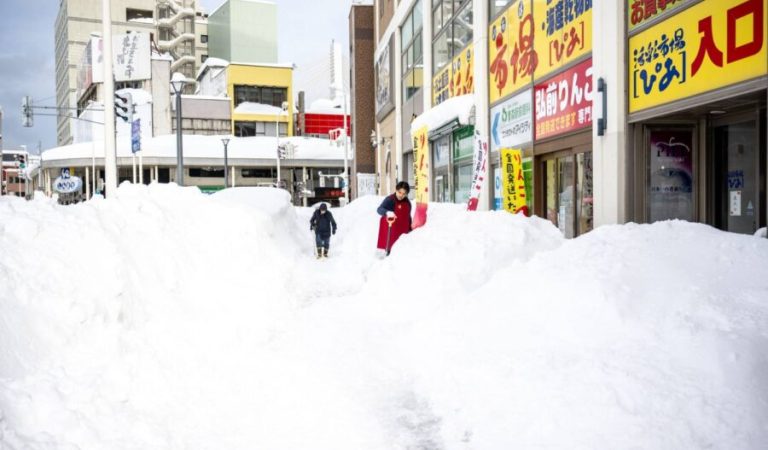 TOPSHOT - A shop employee (R) shovels the snow in front of the shop in Aomori city, Aomori prefecture on January 30, 2026. (Photo by Philip FONG / AFP)
