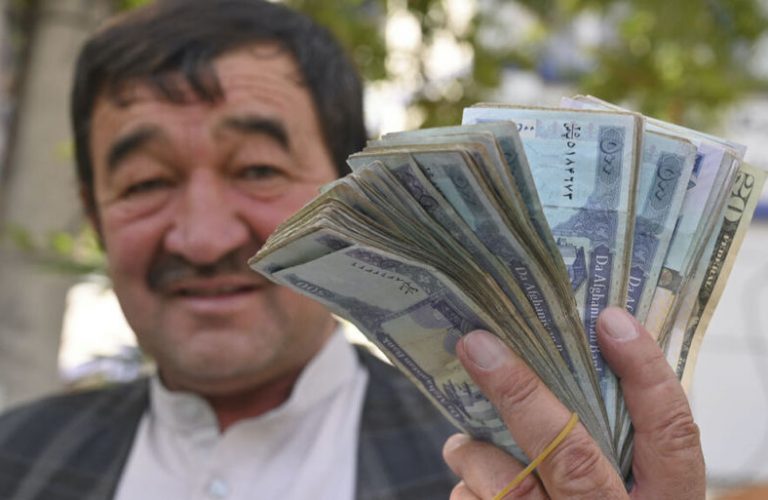 A money changer shows Afghan afghani bills along a street in Kabul on June 30, 2021. (Photo by ADEK BERRY / AFP)
