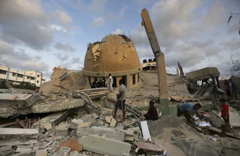 People stand outside a mosque destroyed in an Israeli air strike in Khan Younis, Gaza Strip, Sunday, Oct.8, 2023. The Hamas militants broke out of the blockaded Gaza Strip and rampaged through nearby Israeli communities, taking captives, while Israel's retaliation strikes leveled buildings in Gaza. (AP Photo/Yousef Masoud)