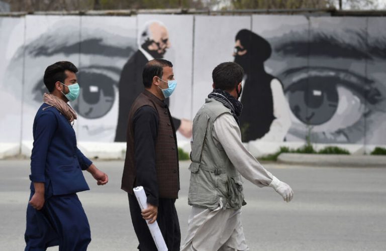 Men wearing facemasks as a precautionary measure against the COVID-19 novel coronavirus walk past a wall painted with images of US Special Representative for Afghanistan Reconciliation Zalmay Khalilzad (L) and Taliban co-founder Mullah Abdul Ghani Baradar (R), in Kabul April 5, 2020. (Photo by WAKIL KOHSAR / AFP) (Photo by WAKIL KOHSAR/AFP via Getty Images)