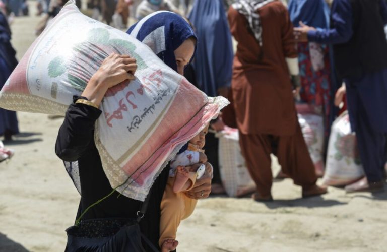 A woman carries her child and a sack of rice distributed to people in need by the Afghan Ministry of Refugees in cooperation with China, in Kabul on June 8, 2022. (Photo by Ahmad SAHEL ARMAN / AFP)