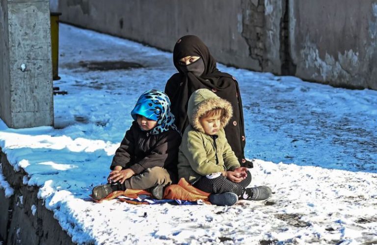 A woman sits with her children along the roadside covered with snow in Kabul on December 16, 2021. (Photo by Mohd RASFAN / AFP)