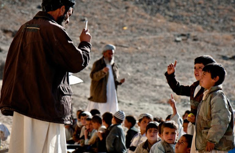 Children ask their teacher questions at an all boys' school in the Tangi Valley, Wardak Province, Afghanistan. As winter neared, in October 2009, the teachers of the school sought building materials from the US Army unit stationed nearby in order to fortify their school; as of October, students were still studying outside. There are no girls schools in the Tangi Valley.